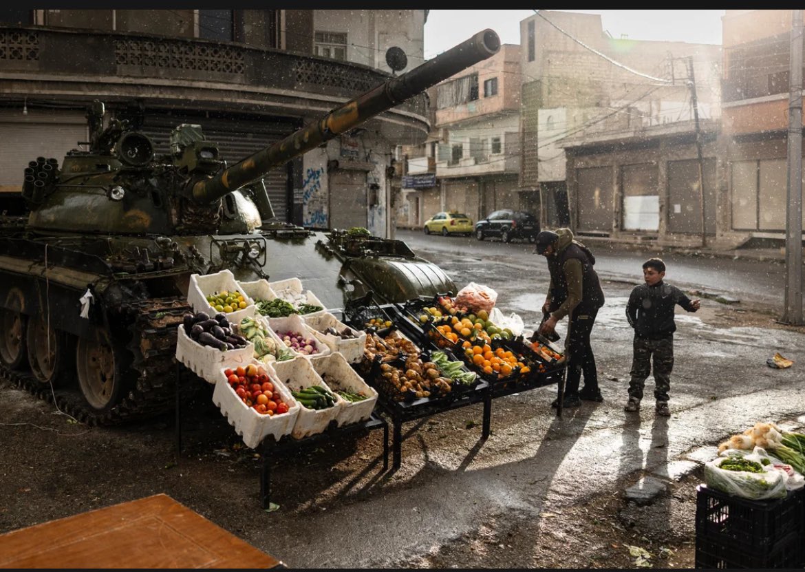 Syria: A man sells fruit in front of damaged tank