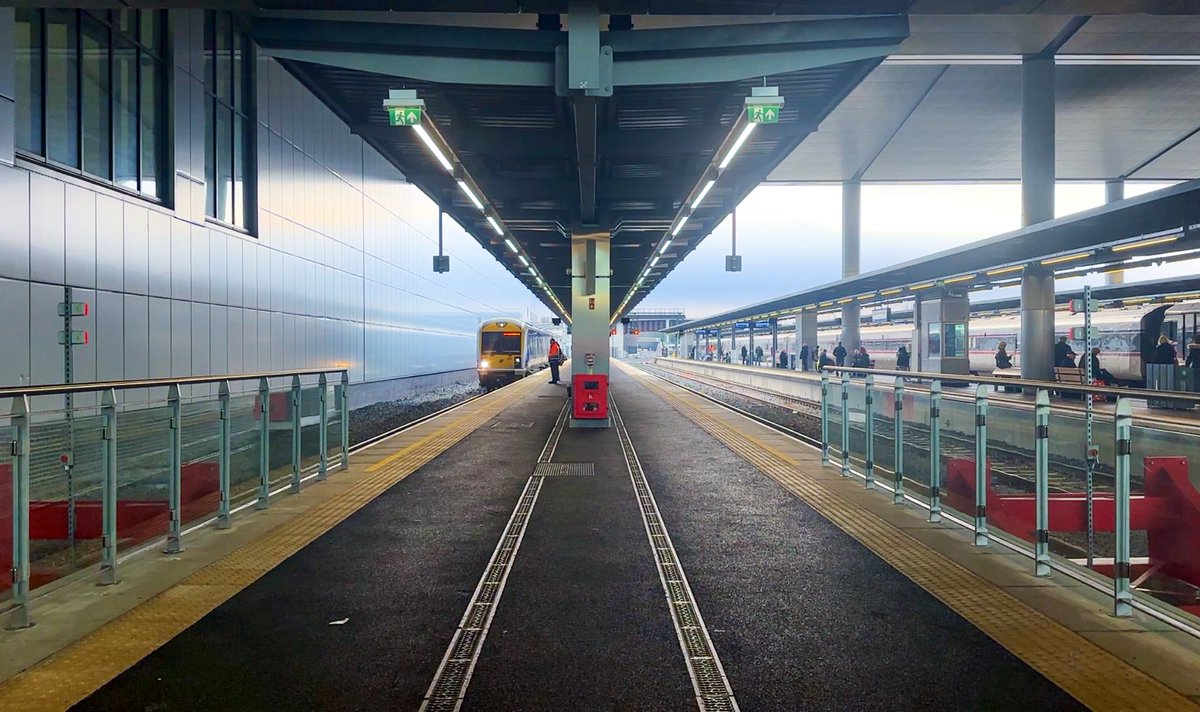 MrTimDunn's tweet photo. I’ve just been to Britain’s newest major city rail & bus terminal - Belfast Grand Central Station - and it’s very good indeed. The city has lacked a decent interchange - or even a decent station - for decades: this is just what was needed. It’s not flashy, it’s bright; it’s not OTT, it’s generous: just like public transport infrastructure should be. “Grand” isn’t the word I’d probably use, but that’s the branding and frankly, it’s grand compared to what Belfast folk had to contend with until now. 

The concourse is huge: enough to deal with sports crowds that surge, and the integration of bus and rail - given how many of those buses replaced train services - is spot on. That great destination board - ace. Road and rail side by side. I also really like the accessible wayfinding - little mini QR codes as coloured blocks on each area, which I’ve never seen in England but it’s an innovation my @networkrail & @RailDeliveryGrp colleagues I hope are looking at implementing. The staff member I talked to about it was very proud of them, anyway.

This week I watched Translink staff welcoming bus passengers with mince pies; others happily giving info and one chap told me I was free to take as many photos of “our terrific new station!” as I wanted. He looked pleased as pie that I asked. He looked proud of it all, too. 

And so they should. NI transport architecture has been dominated by the overbearing shadow of terrorism for decades: whilst this station mightn’t win all the awards for trendy aesthetics, from what I can see so far this is the practical, efficient transport portal to the rest of Ireland and NI that this city needed.  

There’s a shedload of regeneration in this part of town coming as a result, I understand. Interestingly (and as you know I like a good bit of historical referencing in new buildings) there’s an open truss supposedly to reference that of the long-demolished Great Victoria Street terminus which once stood round about here, too. Whether that was planned or post-rationalised I dont know, but it’ll keep me happy for a bit. I haven’t even begun to tell you about the lack of station announcements - it’s a calm space - deliberately not punctuated by superfluous ads or tannoys. VERY GOOD.

So far the only real criticism I’ve seen of it is - laughably - that it’s too big; that it can’t all be needed. I say we need more transport authorities like @Translink_NI - transport operators who invest sensibly for their passengers’ benefit - and for society’s benefit too -  and moreover, confidence and belief in their future and the part that transport plays. Cheers Translink, and nice one @JohnMcAslan et al on its construction.