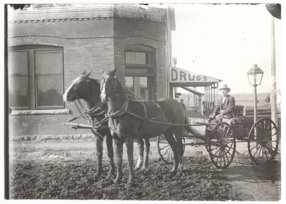 Just horsin' around! 🐎🐴

#SunflowerStamps has us riding through Wilson County, KS on this chilly evening. Here's a glimpse of this man driving his horse-drawn wagon right outside, what looks to be, a drugstore in downtown Benedict between 1890 &amp; 1920.

📷:  <a href="/kansashistory/">Kansas Historical Society</a>
