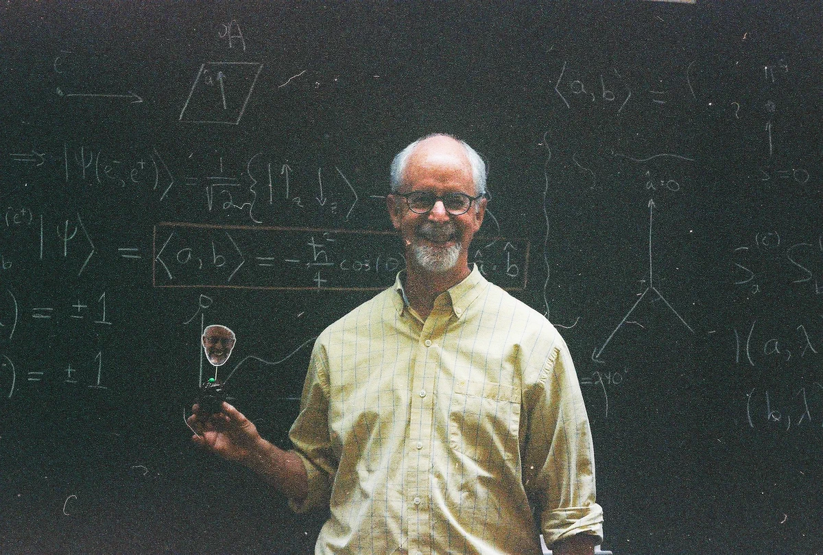 Prof. Glenn Stark in front of a blackboard holding up a cutout of himself