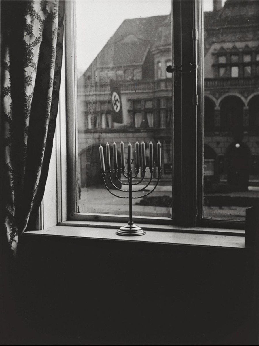 An Chanukkah 1932, kurz vor den Wahlen, die Hitler an die Macht brachten, fotografierte Rahel, die Frau des Rabbiners Dr. Akiba Posner, den Chanukkah-Leuchter der Familie vor dem Hintergrund des gegenüberliegenden Gebäudes, das mit Nazifahnen geschmückt war.

Auf die Rückseite