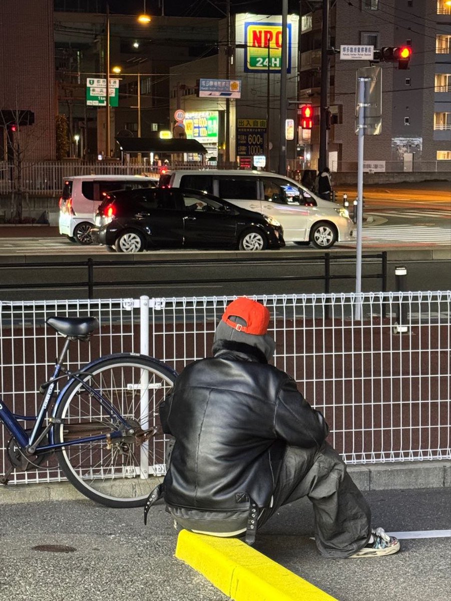 kyunymin's tweet photo. His back turned to the noise, he steps into the calm of solitude, where streetlamps and shadows blur into a personal reverie. The orange his cap, bold against the subdued palette, mirrors the faint flicker of resilience. The bike parked nearby the crossing ahead hint at journeys. https://t.co/LEzqOa7eKj