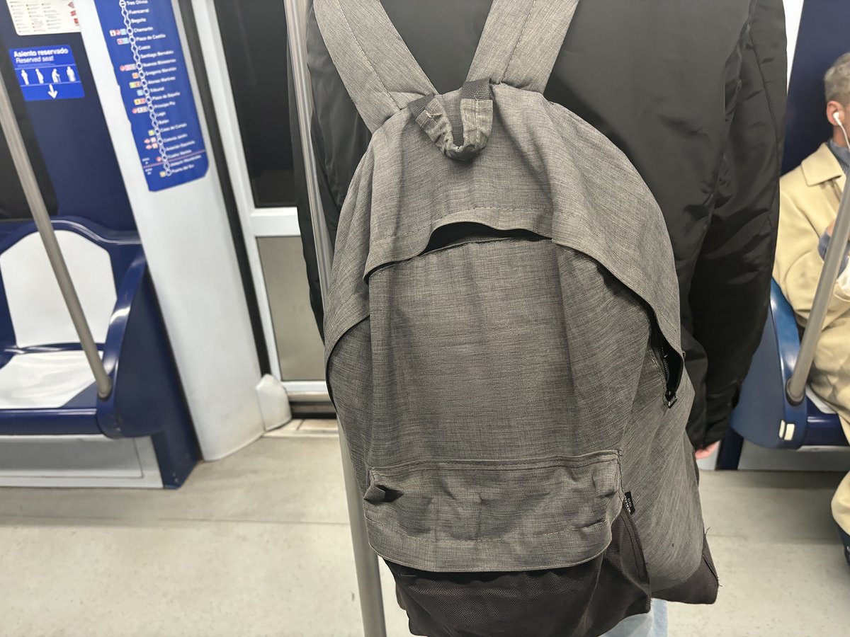 Persona con una mochila a la espalda apoyada en la barra de Metro y otra enfrente con auriculares