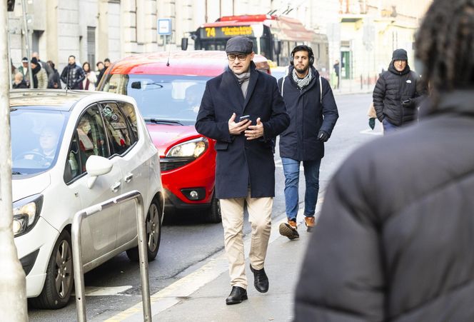 SzwedekM's tweet image. #Challenge1 - „Na zdjęciu widzę ludzi poruszających się chodnikiem oraz jadące samochody. Mężczyzn na pierwszym planie ma na sobie ciemny płaszcz, beżowe spodnie, kaszkiet. W tle widoczne są budynki miejskie i autobus linii 74. Łatwo można potwierdzić, że to Budapeszt” by ChatGPT