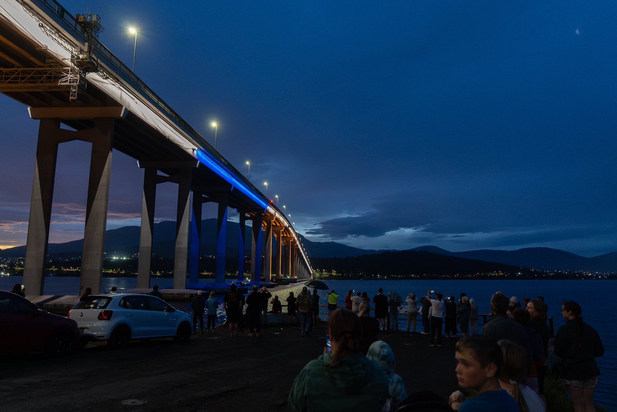 AdamReibel's tweet photo. A solemn ceremony on the Derwent: a lone bagpiper's lament echoes across the water as hundreds watch from the shore. Remembering those lost 50 years ago in the Tasman Bridge disaster, its impact still felt today. https://t.co/rT8MWhY3w0