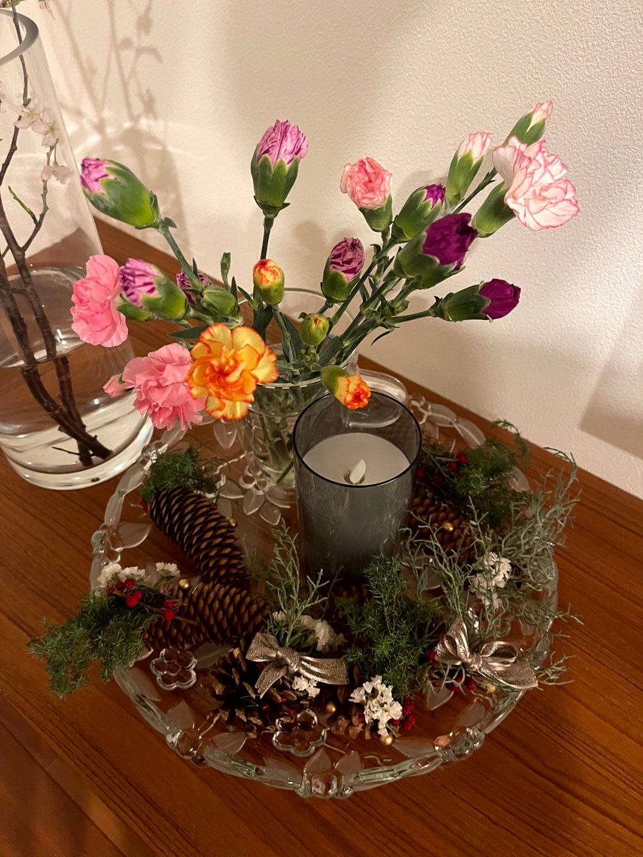 Hiroporin's tweet photo. 冬の花と緑が彩る美しいアレンジメント✨ 色とりどりのカーネーションやバラが、松ぼっくりや常緑植物と調和。中央のキャンドルが温かな雰囲気を演出。季節感溢れる心癒されるインテリアです🕯️🌺🌲 #フラワーアレンジメント #冬の装飾 #インテリア https://t.co/yLXNAa63W5