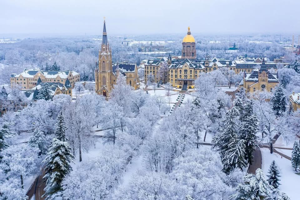 Amid the quiet hush of winter, the University of Notre Dame transforms into a breathtaking wonderland, as captured in this stunning snow-covered scene. The Golden Dome shines brightly, a beacon of hope and tradition, standing tall against the pristine white backdrop. The