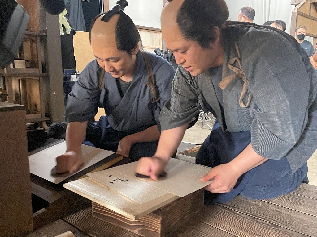 ukiyoe_adachi's tweet photo. 大河ドラマへの出演を通じて、#蔦重 が生きた時代の #木版 の技術が、現代まで続いていることを多くの方に知っていただくことができ、本当に嬉しいです。
写真は、撮影現場で、彫師役・摺師役の役者さんに、道具の扱い方などをお伝えしている新實（にいのみ）と京増（きょうそう）で���。 https://t.co/pHBAaz02N9
