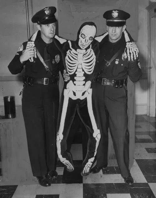 Cops arresting a drunk dude in a skeleton costume, 1950