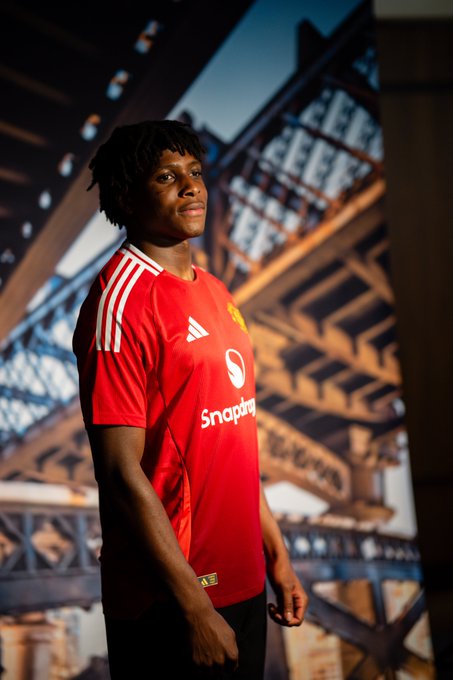 Patrick Dorgu poses in our home shirt in front of a backdrop of Manchester.