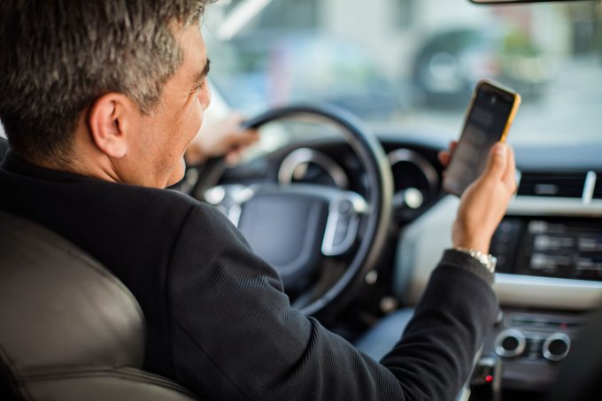 Middle aged man looks at his phone while driving.
