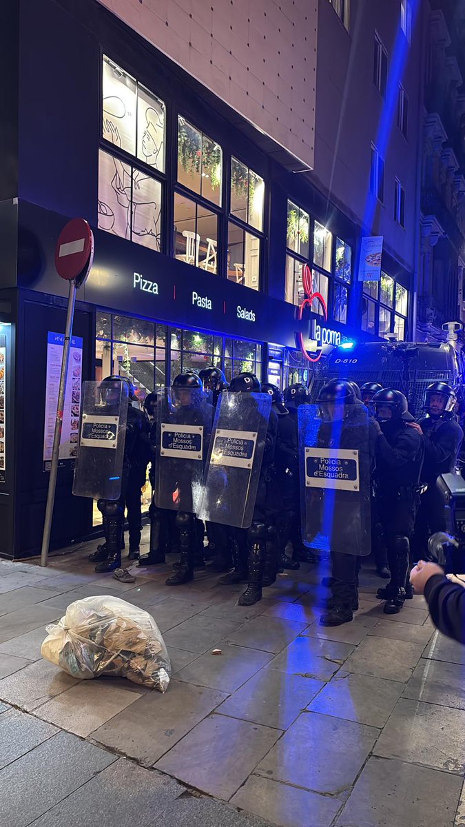 Catinformacio's tweet photo. Dos detinguts per llançar pedres i cremar contenidors durant la manifestació  convocada contra el desallotjament de l'Antiga Escola Massana. També nou Mossos han acabat amb ferides lleus per les pedres i altres objectes que els han llançat. Els manifestants ja s'han dispersat. https://t.co/mqwFeYl1Px