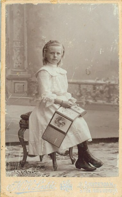 Een meisje, gekleed in een lichte jurk en gezeten op een fraai stoeltje, poseert voor een romantisch decor met een #boek op haar schoot. #collectievissen