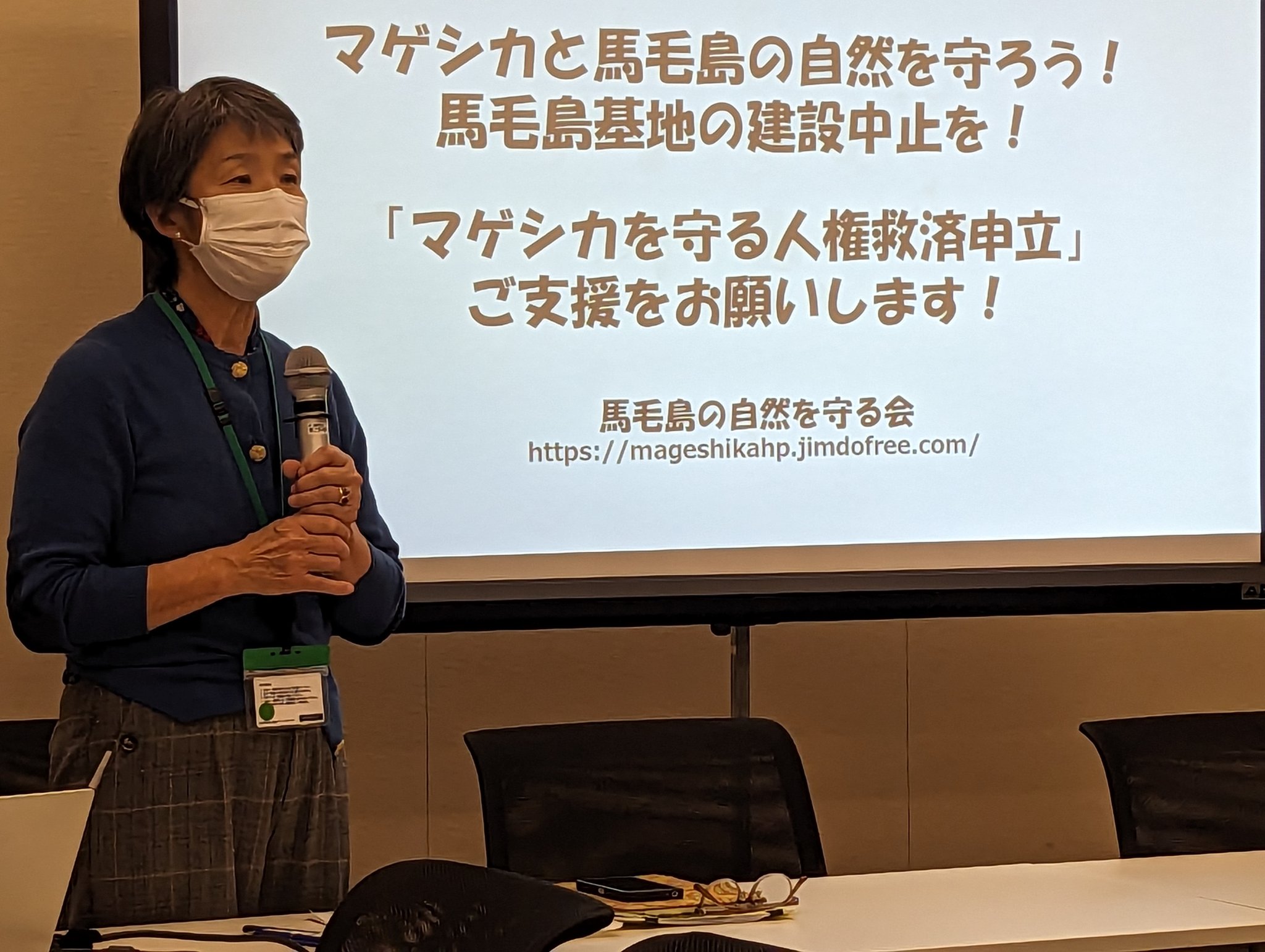 主催者挨拶する長野広美·西之表市議。「マゲシカと馬毛島の自然を守ろう！馬毛島基地の建設中止を！」「マゲシカを守る人権救済申立 ご支援をお願いします！」とのスライド。