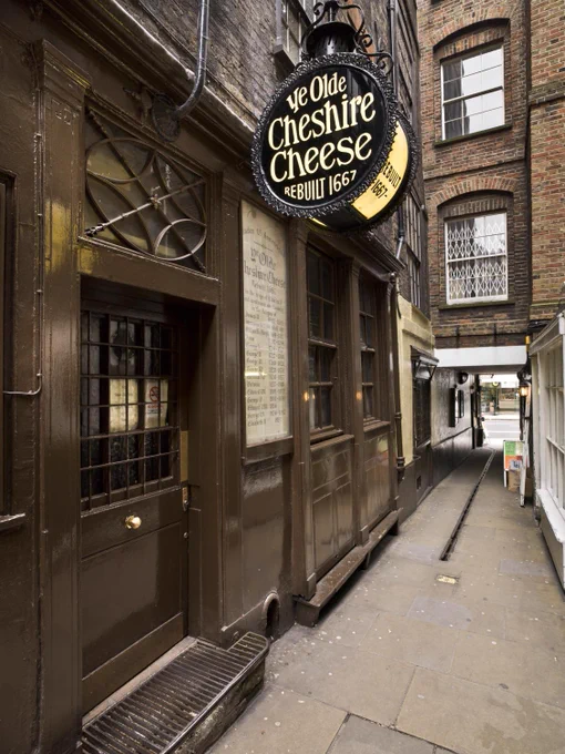 A photo of a small alleyway with a back entrance to a pub with brown painted doors and window frames. A lit-up sign reads, 'Ye olde Cheshire Cheese rebuilt 1667'. 