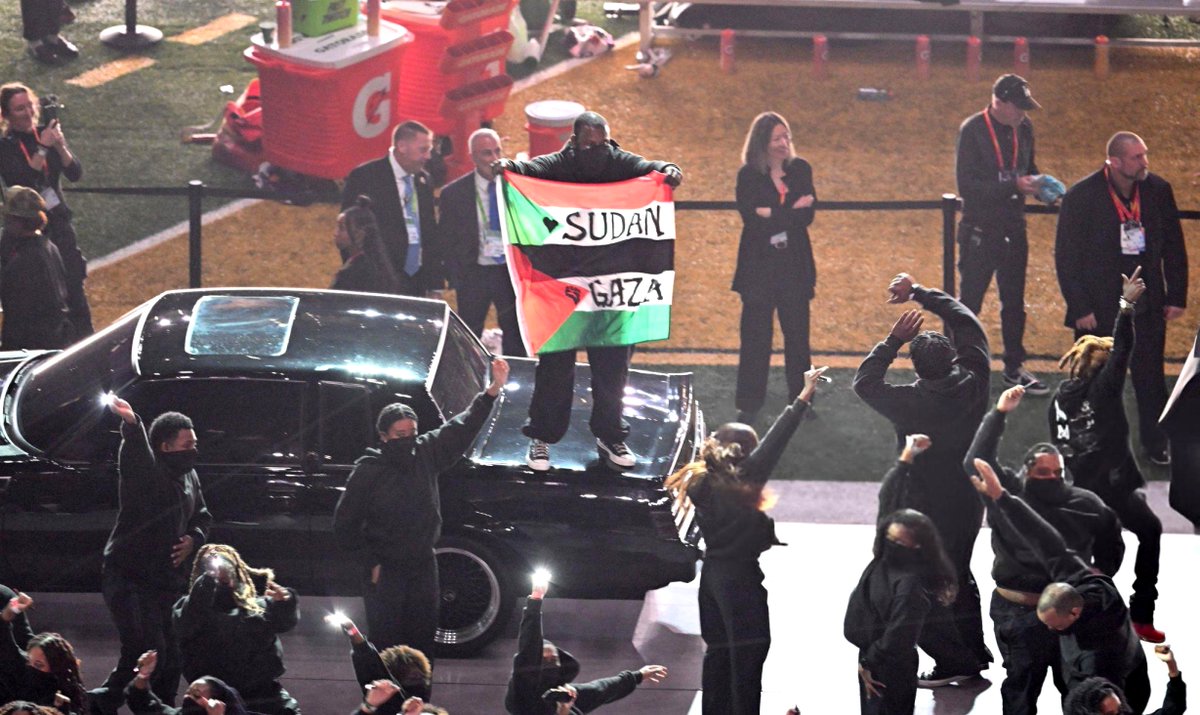 Kurrco's tweet photo. A protestor with a Sudan / Palestine flag made his way onto the stage during Kendrick Lamar's #SuperBowl Halftime Show https://t.co/rNJ6Pd9k6D