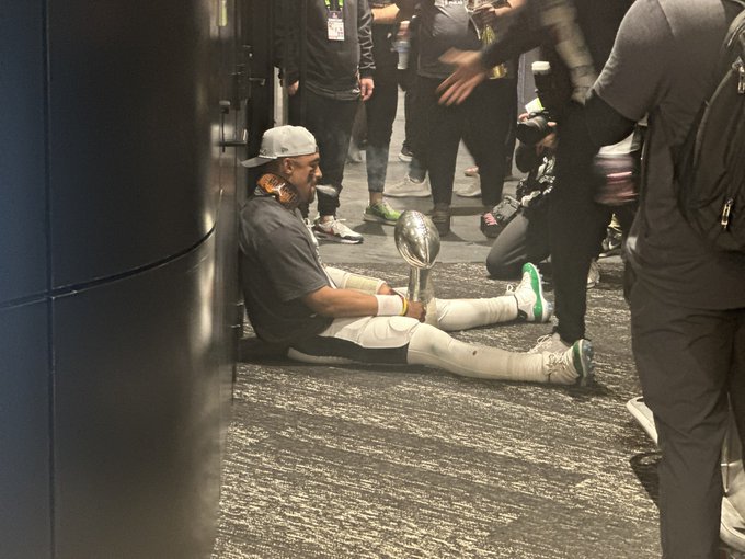 Jalen Hurts sitting on floor looking at trophy