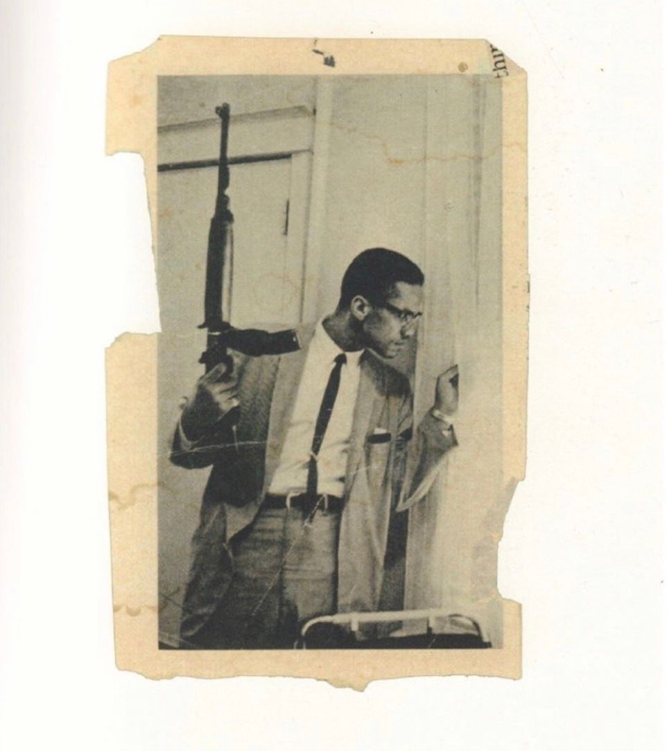 Malcolm X holding an m1 carbine and peering out of his window in response to death threats against him and his family (1964)