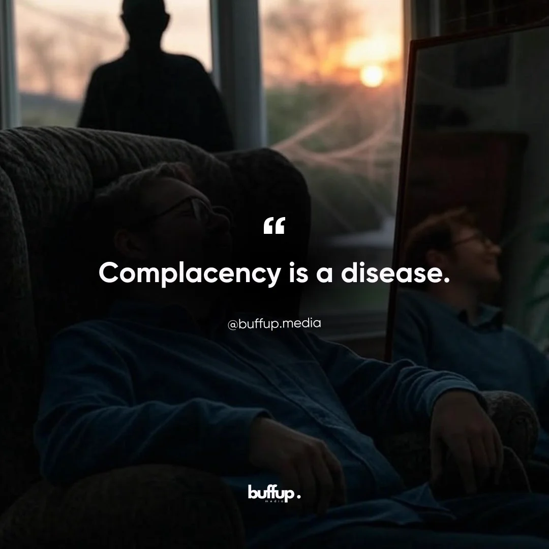 Realistic illustration of a person slouched comfortably on a couch, appearing complacent, with a mirror reflecting their content but unaware face. A shadowy figure looms in the background near a window with a sunset, symbolizing the creeping danger of complacency. The text overlay reads, '“Complacency is a disease.” @buffup.media,' with the Buff Up Media logo at the bottom, representing their message about avoiding stagnation in business.