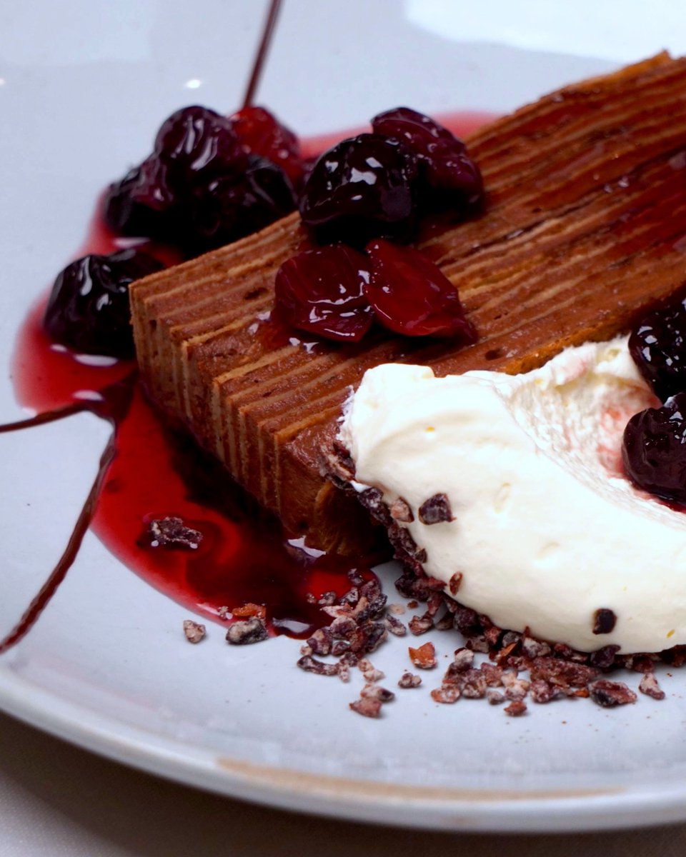 PASTEL DE CREPAS CON CHOCOLATE | 25-layer chocolate mousse-crepe cake, dark chocolate sauce, whipped cream with cocoa nibs, hibiscus-poached Klug Farm cherries.