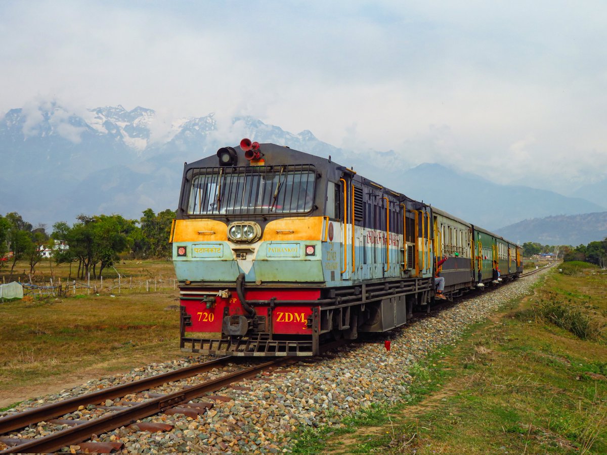 On a cloudy day, the Baijnath Paprola - Nurpur Road passenger speeds towards its next halt, with the picturesque snow-capped Dhauladhar Mountains in the background.

📸 February 2025