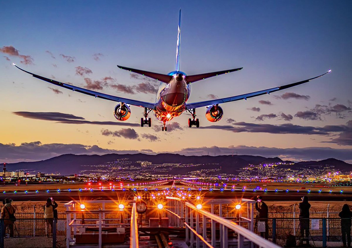As the ANA Boeing 787 Dreamliner descends through 70 feet on final approach into Osaka International Airport, the scene is nothing short of magical. The sunset sky casts a warm glow, painting the horizon in rich hues of orange and pink, while the scattered clouds add texture to