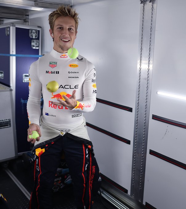 Liam Lawson juggles tennis balls on the Oracle Red Bull Racing truck in his race suit.