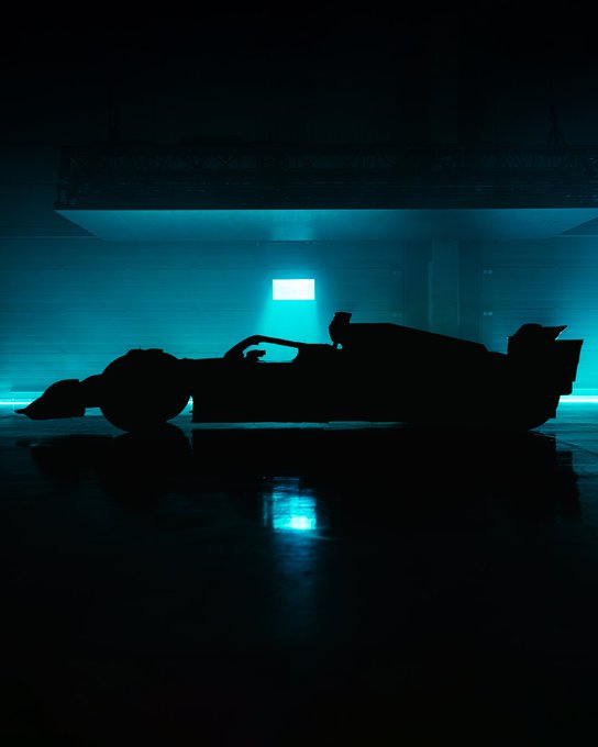 A dark garage environment with blue backlighting and a silhouette of an F1 car in the middle of the frame. 