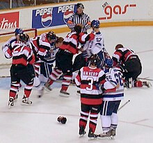 two hockey players holding each other as a brawl happens in front of them on the ice