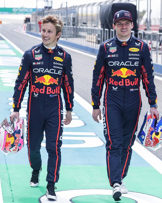 Liam and Max walking down the pit lane in their race suits with their helmets.