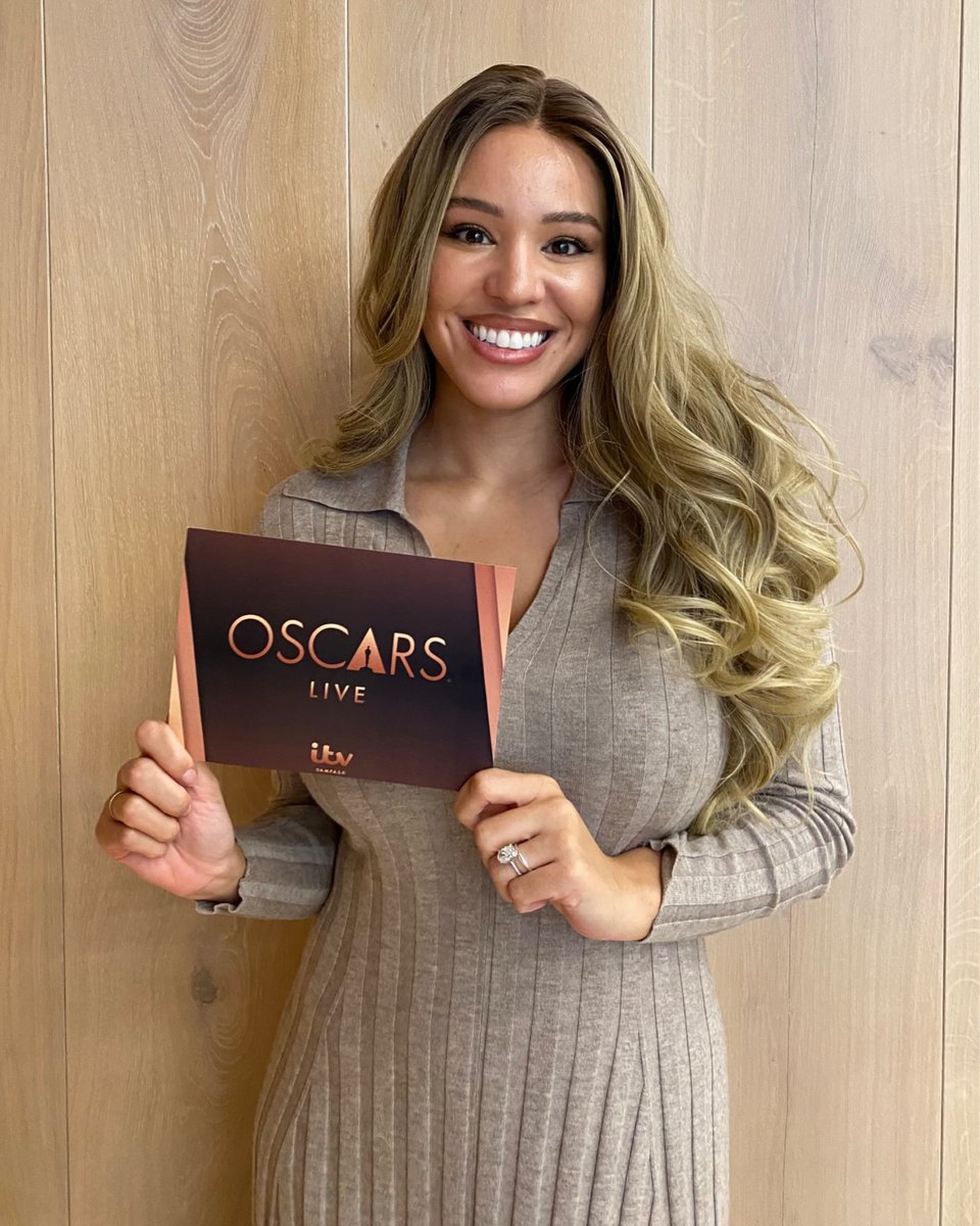 A smiling mixed race black woman holds a cue card reading “Oscars LIVE, ITV”