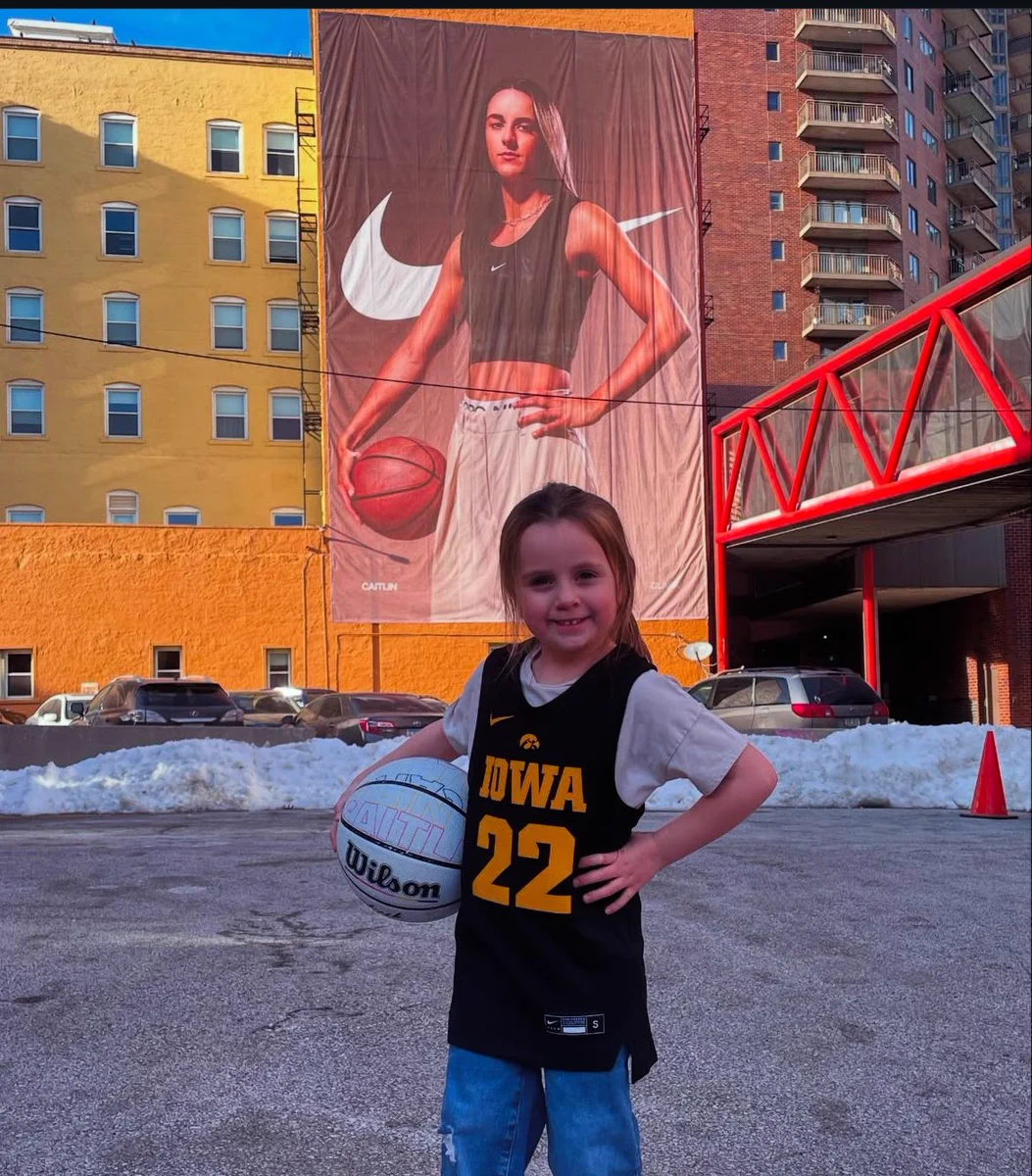 Photo of a little girl posing in an Iowa jersey, in front of a Caitlin Clark Nike banner.