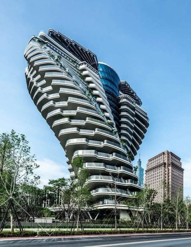 The building pictured is called Tao Zhu Yin Yuan, also known as Agora Garden, located in Taipei, Taiwan. It is a residential high-rise designed by Vincent Callebaut Architectures and was completed in 2018. The building's design is inspired by the double helix structure of DNA