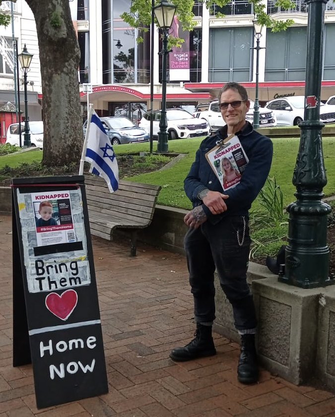IndigenousCFI's tweet image. This is Edi. Several times a week he sets up his stand in the center of Dunedin to raise awareness of the Israeli hostages. On several occasions he has been assaulted and his flag ripped from its stand. He has been spat at, screamed at and sworn at. On one occasion two young men…