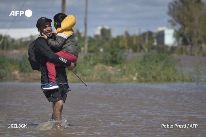 A man carrying a child walks through flooded waters in Bahia Blanca, on March 8, 2025.