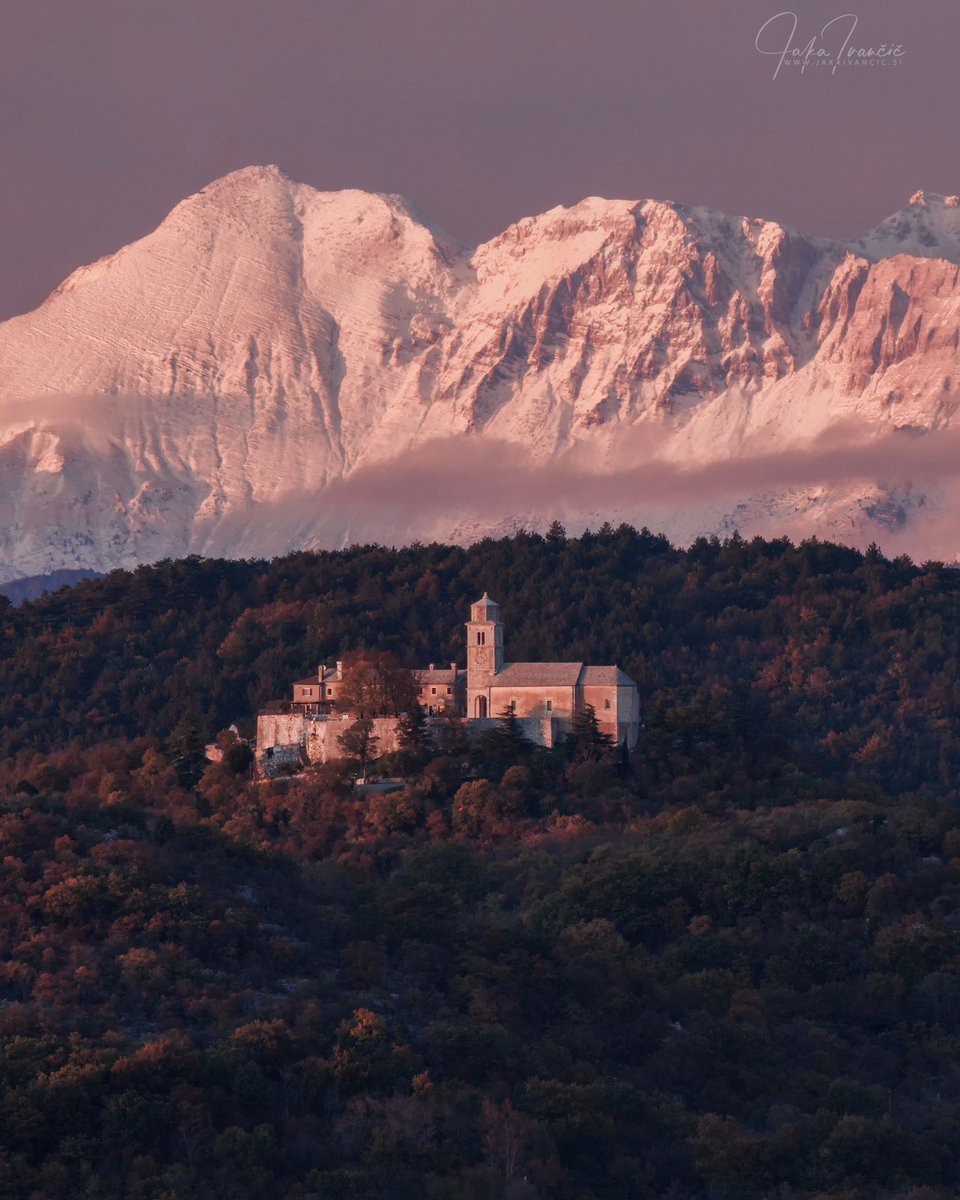 A breathtaking view over the Karst plateau with Repentabor (Monrupino) stands illuminated by the warm light of sunset. In the background, the snow-covered peaks of the Slovenian Alps complete the scene, blending the landscapes of both Italy and Slovenia.