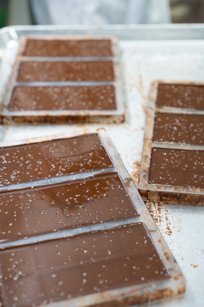 Inclusions are added after the liquid chocolate is poured into a mold and then hand sprinkled on top. Here, a chocolate maker at Moka Origins puts the finishing touches on these chocolate bars.