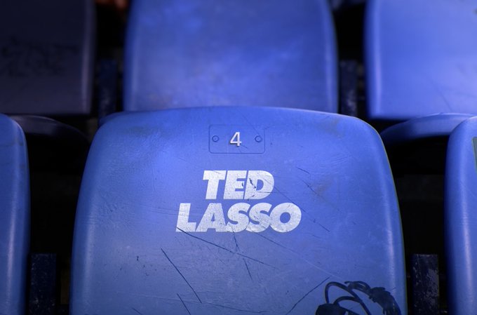 From Ted Lasso. This photo showcases a blue chair in a set of bleachers that reads the number 4 above the "Ted Lasso" logo.