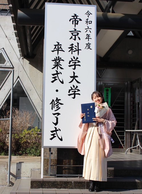 The first image captures a graduation ceremony at Tokyo Budokan, as indicated by the post text. A young woman, presumably Azusa, the team captain mentioned in the post, is standing in front of a large vertical banner with Japanese text that reads "帝京科学大学 卒業式" (Teikyo University of Science Graduation Ceremony). She is dressed in traditional academic attire, holding a diploma, and smiling warmly, reflecting the celebratory mood of the event. The setting is outdoors, with modern architectural elements visible in the background. The second image shows a group of young women, likely members of the Teikyo University of Science Women's Ekiden Team, posing together on a sports field. They are dressed in athletic wear, with one individual in the center also in graduation attire, holding a diploma. The group's cheerful expressions and hand gestures suggest camaraderie and support, celebrating the graduation of their teammate. The post text conveys gratitude towards Azusa for her leadership and wishes her success in her future endeavors in a corporate team.