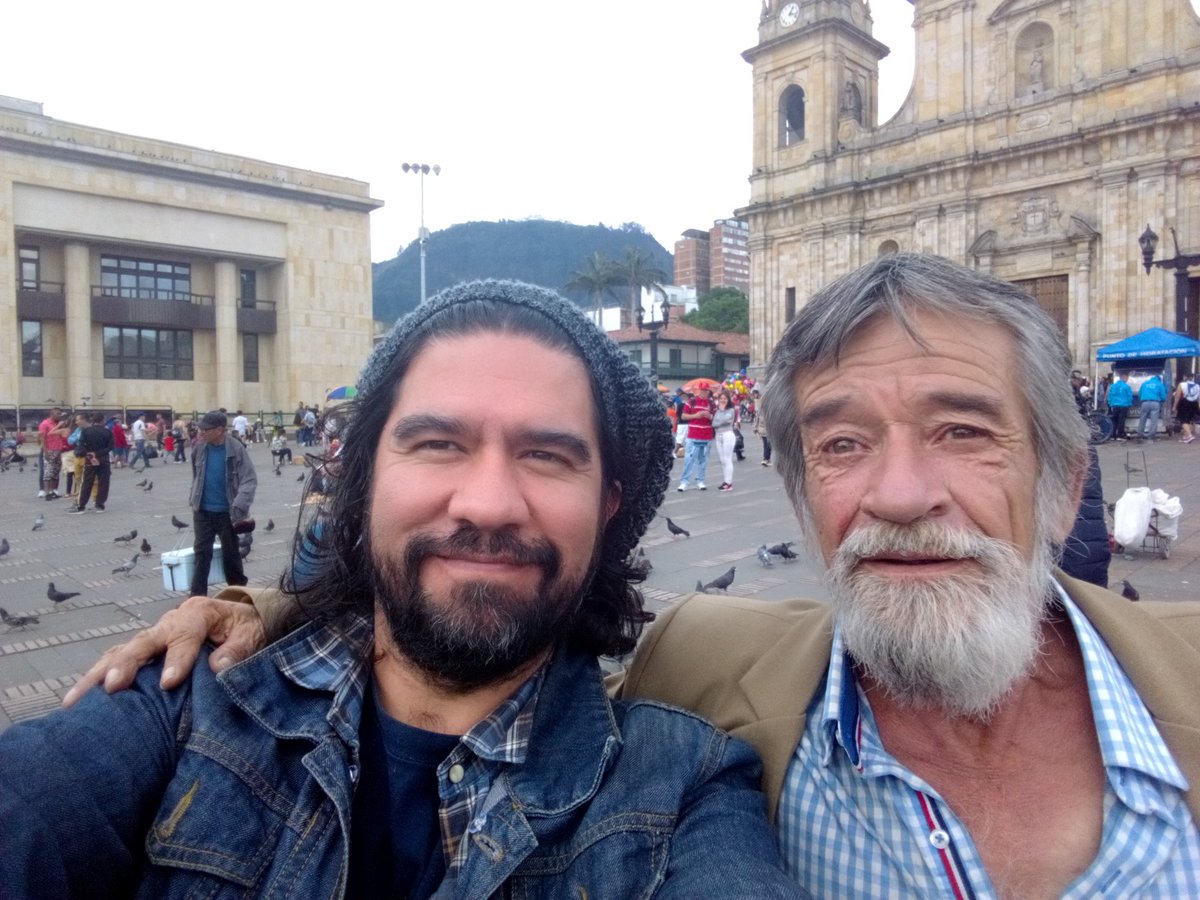 altereddie's tweet photo. Ya que es el día de la felicidad, les comparto una pequeña historia que escribí hace varios años sobre mi amigo Fermín a quien le agradezco sus reflexiones sobre la felicidad. Ya Fermín no es habitante de calle y sigue viviendo en su amada Tunja.

Tunja. Son las 7 de la mañana. Camino por la plaza de Bolívar junto a la famosa esquina de la pulmonía. Hace un frío de esos cargados de viento congelador. Escucho una voz que canta a todo pulmón “la felicidad, ja, ja, ja, ja, de sentir amor, jo, jo, jo , jor, hoy hacen cantar, ja, ja, ja , jar, a mi corazón”, voy en busca del cantante y lo encuentro allí, sentado en una acera. Le dejo unas monedas y me saluda con una sonrisa. Durante todo el día me quedo con el coro de esta canción de Palito Ortega. Me pregunto repetidamente qué es la felicidad para este hombre, pues quede contagiado con las estrofas de la felicidad desde la mañana. Tengo un día de esos de once sobre diez.
Al día siguiente lo busco nuevamente. Le cuento que tuve un día muy feliz gracias a sus coros, me dice “con mis canciones yo le emano energía positiva a la gente, me la gano cantando y no como los políticos que lo hacen robando”.
Fermín López es su nombre, es de Sogamoso y tiene 62 años.
Me dice que lleva en la calle veinte años, que su papá fue uno de los fundadores de acerías Paz de Río y que vivió en Alemania durante cinco años. Cuenta que se accidentó en su trabajo como ingeniero civil y durante un tiempo estuvo en estado de coma, le dio amnesia y se le desconectaron los cables,”dos cablecitos de la cabeza” que lo dejaron con problemas, por esto terminó en la calle y por decisión propia no quiso ser un encarte para su familia.
¿Fermín, usted se considera feliz? Claro, completamente feliz, soy amigo de los que pasan por estos lados, de abogados, concejales. Llego aquí y me voy  a la hora que se me da la gana, no marco tarjetas para nadie, vivo a la salida de la ciudad en un bosque y convivo con la naturaleza, con los animalitos, no le debo nada a nadie. Me da tristeza de esos políticos a los que les toca andar de un lado para otro en carros blindados y que hasta para ir al baño necesitan escoltas. Yo soy libre y canto porque estoy feliz, le animo el día a más de uno.
Lo malo de vivir en la calle es que uno tiene que cuidarse de las operaciones de limpieza social, yo me he salvado de más de una, ¡limpieza social, eso deberían empezarlo por las alcadías, las gobernaciones y el congreso lleno de ladrones! ¿Cuál es el pez favorito de los políticos? el róbalo, je, je.
Ahora Fermín canta “tu tienes una carita deliciosa, despeinada, ja, ja, ja, ja”. Le gustan las canciones de los sesenta y los setenta, Palito Ortega y Leonardo Favio son sus cantantes favoritos.
Fermín es un amante de Tunja, habla maravillas de la ciudad “¡Frío! ¡frío en Alemania, con esos días corticos y nieve por todo lado y sin ver el sol, eso sí es frío, aquí no llega el chikunguña ni ese tipo de bichos, no llegan ni los chulos, bueno algunos pero vestidos de sotana. Tunja no tiene ladrones, excepto los curas y los políticos, es una ciudad muy sana. Aquí el agua es de lo mejor, limpiecita. Los tunjanos tienen fama de asolapados pero yo no creo eso, me gusta la gente de por aquí, es muy buena. Las universidades también son de lo mejorcito”.
Le cuento a Fermín que tengo una exposición en la casa de la cultura y lo invito a que vaya conmigo. Fermín sonríe y me acompaña. Observa las fotografías de habitantes de calle en Los Angeles mientras yo le pregunto si le gustaría posar para que yo lo haga, el me dice entusiasmado que sí, que él es un personaje de la ciudad.
Hacemos una pausa mientras él se toma un café y yo voy por mi kit personal. Traigo mis plastilinas y empiezo a modelarlo. Mucha gente se acerca mientras Fermín, sentado, habla y habla echándole vainazos a todos los que ve por allí con cara de empleados oficiales. Ríe a carcajadas, cuenta anécdotas de su vida, habla de política.
Yo mientras tanto detallo sus zapatos negros gastados y empolvados. Modelo su costal de harina cargado de sus no se ques, su piel enrojecida por el sol y endurecida por el viento, sus manos arrugadas, su chaqueta de cuero, su saco lleno de motas, su vestido de paño barato color café, su reloj inmenso, sus ojos rosados y verdes, sus arrugas pronunciadas en la cara, su barba con infinitos matices de gris, su gorra con un estampado que parece el graffiti de algún pintor callejero confundido.
La gente lo escucha y me observan trabajar. Pasa una hora y cuando Fermín ve su escultura en plastilina sonríe y me felicita, me señala y le dice al público “este es todo un artista”. Nos abrazamos y nos tomamos fotos para la prensa, la televisión y todos los curiosos que ven en este encuentro algo poco común.
Ahora la gente se toma fotos con Fermín, le preguntan todo tipo de cosas, miran al muñeco, lo miran a él. Es el personaje central de la exposición.