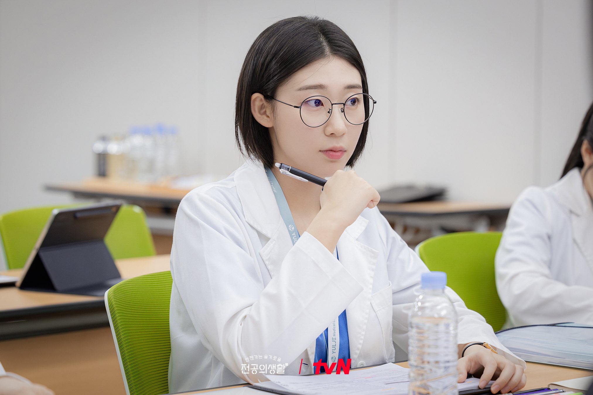 Karakter Resident Playbook, Kim Sa-bi, sedang memegang pulpen dan buku catatan di tengah-tengah belajar