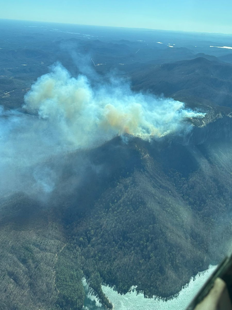 ForestryCommish's tweet photo. TABLE ROCK FIRE UPDATE – PICKENS COUNTY SC – 18:00:00 –MARCH 22, 2025

The Table Rock Fire, which ignited Friday, is estimated at 35-plus acres and continues to grow. While more than 30 personnel from the South Carolina Forestry Commission, The Nature Conservancy, Greenville Water, the USDA Forest Service and local fire departments are working to contain the fire, the steep, mountainous terrain is making it difficult for firefighters to access the active fire and establish more effective firebreaks.

Several spot fires – when embers land on the unburned side of a fireline – have led to new ignitions outside of the original fire area. Exacerbating the situation is an abundance of downed timber from Hurricane Helene, which has increased the fuel load on the mountain. Fire weather conditions have continued to deteriorate today, with wind gusts increasing, and relative humidity dropping below 20%.
Four aircraft have been providing aviation support all day, including one SCFC airplane surveying the fire, two SCFC single-engine air tankers dropping water and one SLED helicopter using a Bambi bucket to drop water. Officials are hoping to add more air resources tomorrow as the situation evolves.

REMINDER: A statewide burning ban issued yesterday at 6 p.m. remains in effect until further notice. A State Forester’s Burning Ban prohibits all outdoor burning, including yard debris burning, prescribed burning, campfires, bonfires and other recreational fires in all unincorporated areas of the state.

FIRE BACKGROUND: Human-caused / March 21, 2025 / Table Rock State Park, 13 miles north of downtown Pickens, SC

FIRE SIZE: 35+ acres, as of March 22, 2025

CONTAINMENT: 0%

EVACUATIONS: Out of an abundance of caution, local fire officials are calling for voluntary evacuations of residents who live on eight roads in close proximity to Table Rock Mountain. Those roads are:
-Country Creek Drive
-Weaver Creek Trail
-Katijah Lane
-Lynne Way
-Dry Lake Road
-Curtis Way
-Shepherd Springs Drive
-Gnome Hill Lane 

Officials are going door-to-door to make residents aware of the call for voluntary evacuations and also working to establish a nearby evacuation center yet to be determined. Residents on these roads are not in immediate danger, but are being notified of the possibility of the eventual spread of the Table Rock Fire to their vicinity.

ESTIMATED COSTS TO DATE: N/A

FIRE CREWS/RESOURCES:  More than 30 personnel from the South Carolina Forestry Commission, The Nature Conservancy, Greenville Water, the USDA Forest Service and local fire departments. Four aircraft, including one SCFC aerial observer, two SCFC single engine air tankers and one SLED helicopter.

INJURIES: No injuries have been reported.

STRUCTURES: No structures are threatened at this time.

CLOSURES: Table Rock State Park trails are closed until further notice. 

UPDATES: Updates will be provided only as new information becomes available; nightfall will limit additional containment/suppression operations until morning.

PHOTOS/VIDEOS CREDIT: SCFC Piedmont Region Pilot Lee Berry