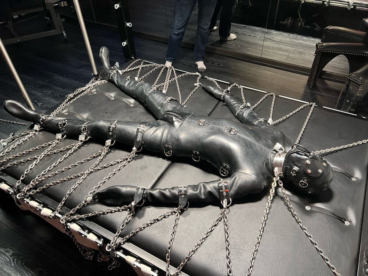 bondagefan70's tweet photo. Rubber slave @bondagefan70 helplessly bound by @SFDom and @MarkBurnley in a high-end bondage rubber suit, gagged and breathcontrolled with heavy chains to a bondage bed. 
More at https://t.co/QQE3H30nqO @seriousMBondage and https://t.co/Onmv0DAKPK .
#rubbersuit # bondage # breathcontrol