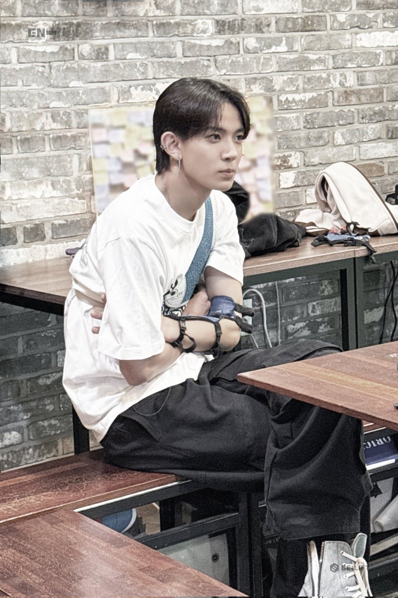 He’s looking straight-up fire, rockin’ that white tee with a dope graphic while pullin’ back the bow like a pro in this cozy café vibe. That archery gear’s got him flexin’ a whole new level of cool, with focus so sharp he’s basically a heartthrob sniper.