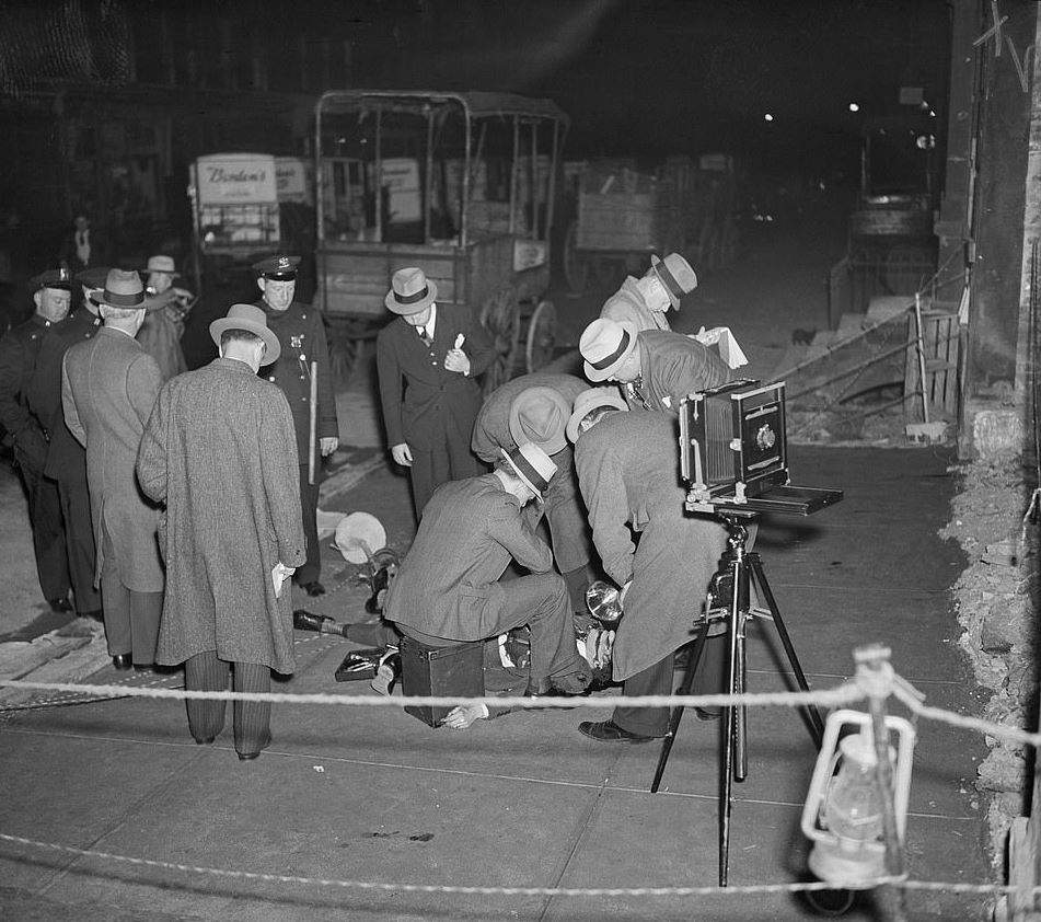NYC Detectives at the scene of the murder of Johnny La Polla, a Bronx policy operator, who was hit by 3 gangland bullets while walking on East 102nd street, at 3 A.M. on May 21, 1937. His enemies, police said, were many. He'd been arrested 11 times, &amp; was sought for a shooting.
