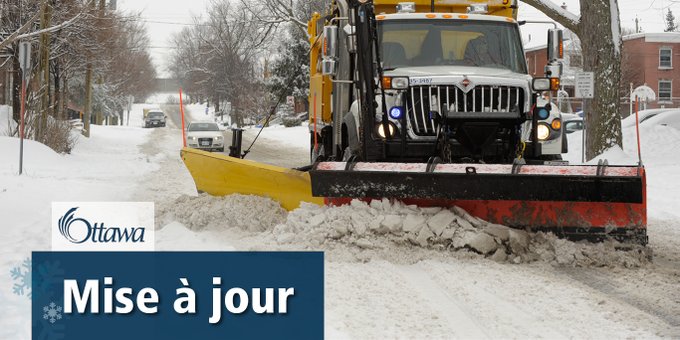Un chasse-neige de la ville d'Ottawa roule dans une rue avec le chasse-neige baissé pour déneiger la chaussée. Un encadré bleue dans lequel sont écrits les mots : « mise à jour » se trouve dans le coin inférieur gauche.
