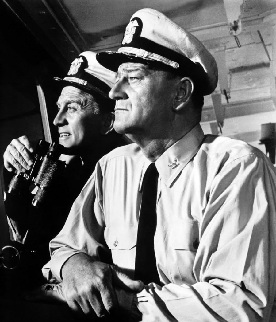 JuanmadelaPoza's tweet photo. #JohnWayne y #KirkDouglas en una fabulosa fotografía publicitaria de #PrimeraVictoria (#InHarmsWay, 1965), de #OttoPreminger. Se cumplen 60 años del estreno de una de las obras maestras del cine bélico. La película reunió por segunda vez a John Wayne y #PatriciaNeal después de #LaFotaSilenciosa (#OperaciónPacífico, 1951), de #GeorgeWaggner. «Primera victoria» fue la primera de las tres películas que John Wayne y Kirk Douglas rodaron juntos. En 1964, rodando «Primera victoria» en Hawái la tos de John Wayne se volvió tan fuerte que Otto Preminger tuvo que interrumpir el rodaje en varias ocasiones. El Duque insistió en que todo estaba bien y todo continuó como si nada hubiera pasado. A John Wayne se le diagnosticó cáncer de pulmón cuando finalizó el rodaje. En el momento de su estreno la película fue ridiculizada por la mayoría de los críticos, quienes la vieron como un intento fallido de emular el éxito de #DeAquíALaEternidad (#FromHereToEternity, 1953), de #FredZinnemann. Varios críticos señalaron que John Wayne era demasiado mayor para interpretar a Rockwell W. «Rock» Torrey, un capitán de la Marina de los Estados Unidos en la #SegundaGuerraMundial. También criticaron duramente que la película pusiera su foco de atención en el personaje interpretado por John Wayne. Aunque no cumplió las expectativas en la taquilla ni se consideró un clásico cuando se estrenó, «Primera victoria» ha ido ganando seguidores con el paso de los años, convirtiéndose en una película de culto. Muchos cinéfilos creemos que John Wayne realiza una de sus mejores interpretaciones, despojada en muchas ocasiones de su personalidad de tipo duro. Durante la mayor parte del metraje el actor interpreta a una persona vulnerable en lugar de a un héroe de acción. «Primera victoria» solo tuvo una nominación en la 38.ª edición de los #PremiosÓscar: mejor fotografía en blanco y negro (#LoyalGriggs). Muy pocas veces el cine bélico adquiere una dimensión tan noble, convirtiendo a sus héroes en seres humanos verdaderos, y fundiendo sus conflictos interiores con un profundo amor al deber (la patria, en este caso). Personajes que asumen los valores del sacrificio, el esfuerzo, el deber, la lucha, siempre determinantes en un conflicto bélico, en conjunción a los sentimientos y emociones profundas de hombres y mujeres que ansían llevar una vida de ciudadanos normales. Los entresijos, interioridades y miserias del mundo militar están muy bien reflejados en «Primera victoria», con sus envidias, pequeñas traiciones y afectos profundos. Los dos personajes principales están muy bien profundizados. John Wayne, honorable como siempre, es degradado a capitán mientras mantiene un idilio con una enfermera (Patricia Neal), que a su vez conoce a su hijo (#BrandonDeWilde). Kirk Douglas vuelve a interpretar, como en la mayoría de sus películas, a un antihéroe, quizá eso es lo que hace de él un actor tan peculiar y llamativo. El resto de actores también están muy bien. Destacar la presencia del gran #HenryFonda, que, aunque sale muy poco, aporta un aire fresco a la película. Las escenas de acción están muy cuidadas y los exteriores rodados en Hawái son bastante bellos. La música de #JerryGoldsmith hace el resto. En «Primera victoria» el capitán Rockwell Torrey y el comandante Paul Eddington forman parte de un destacamento de la Marina estadounidense cuya misión es responder al ataque perpetrado por los japoneses contra la base americana de Pearl Harbor. Torrey, enamorado de la enfermera Maggie Haynes, intenta mejorar la distante y tensa relación con su hijo Jeremiah, un joven oficial de la Marina.