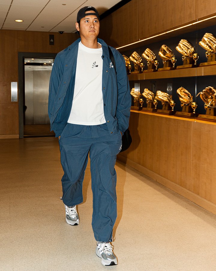 Shohei Ohtani walking into Dodger Stadium. He's wearing a backwards black hat, blue jacket, white shirt, blue pants and white shoes.
