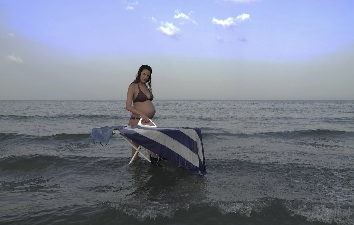Ironing a Greek &amp; EU flag in Cy. In 2004, the whole of Cy entered the  EU even though 38% is still occupied by Turkey. Ironing signifies her Hellenic identity and heavily pregnant on the shores of Cyprus signifies care, the foundational fabric of social reproduction <a href="/LiaLapithi/">Lia Lapithi</a>