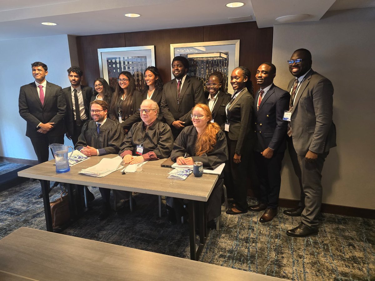 uculaw's tweet image. Preliminary Rounds 1: Team Uganda takes a photo with the Judges and Team 465 after the first preliminary round. Our team was represented by Kylie E. Kukunda, Abraham B. Wanyanga, and Stuart Ssemwogerere as Of Counsel.